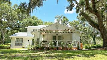 A two-story house with a porch, surrounded by trees and greenery.