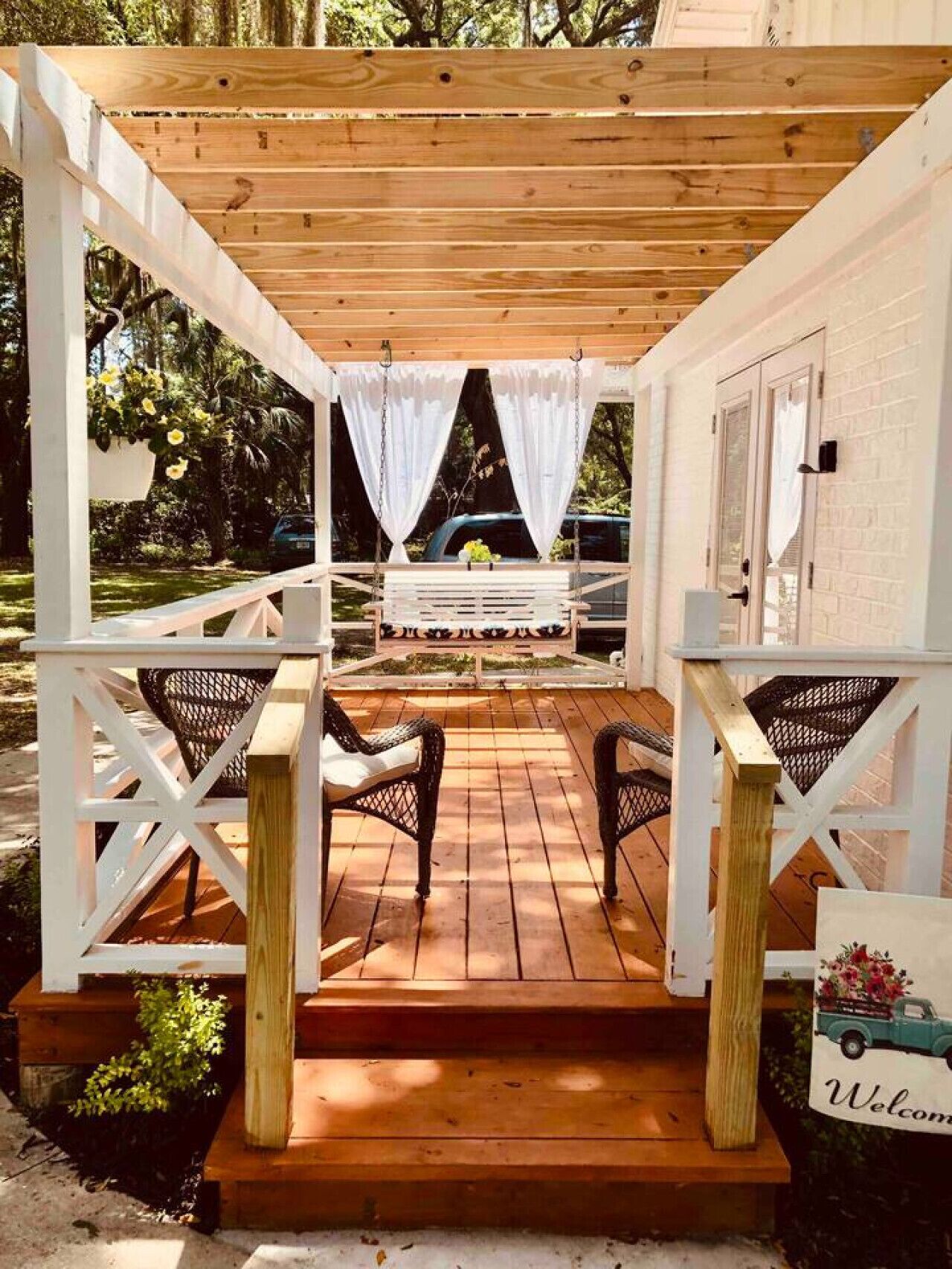 A wooden deck with a covered seating area, white railings, and a welcome sign.