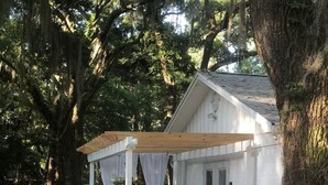 A white wooden structure with a covered porch, a small porch area with a bench, and a sign with a vehicle image. - French Cottage Studio • Dog-Friendly • Near Amelia Island (Fernandina Beach)