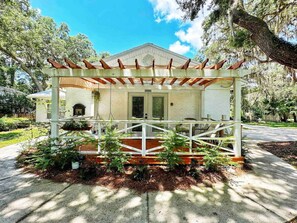 A house with a covered porch, a small garden, and a pathway leading to the entrance. - French Cottage Studio • Dog-Friendly • Near Amelia Island (Fernandina Beach)