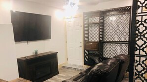 Een woonkamer met een flatscreen-televisie aan de muur, een leren bank, een salontafel en een deur met een patroon.