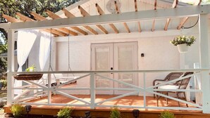A covered outdoor area with a wooden deck, a swing, and a seating area with chairs.