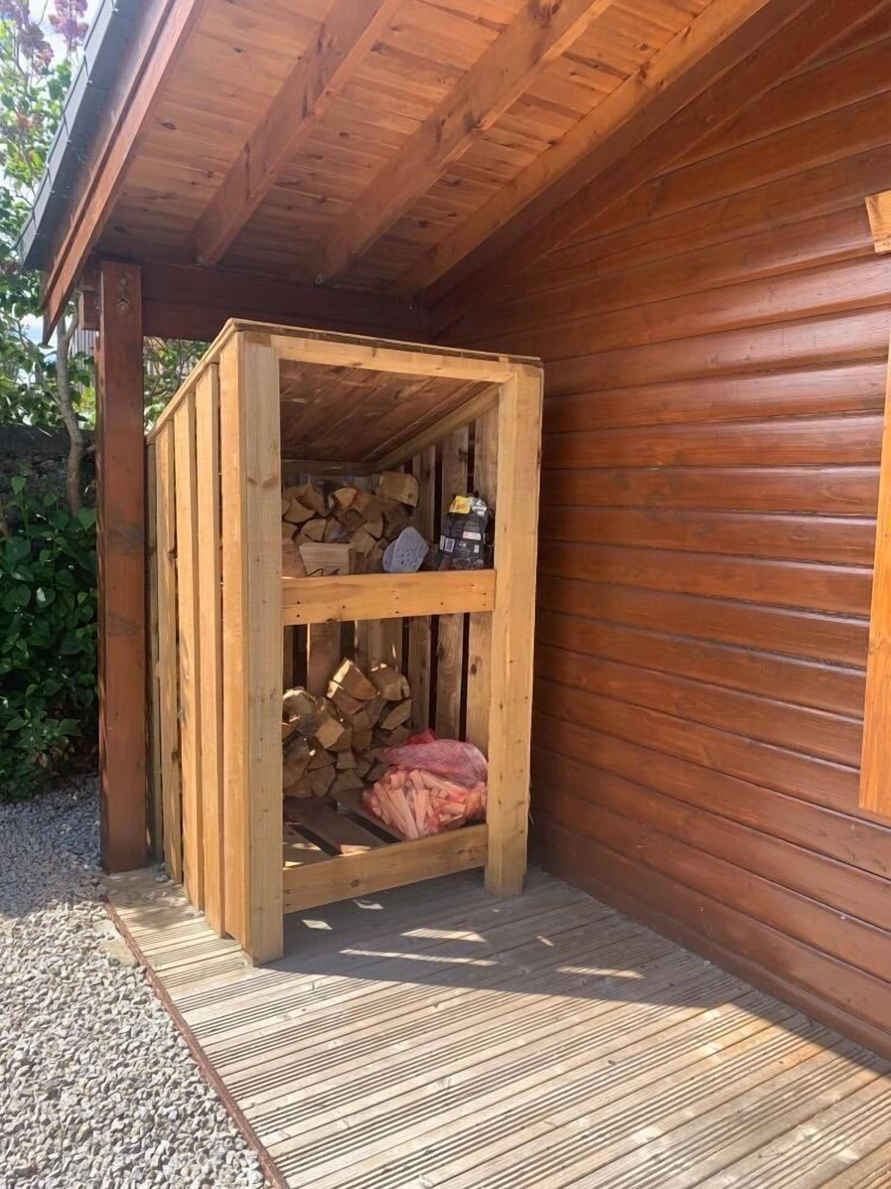 A wooden structure with a sloped roof, a wooden bench, and a stack of firewood.