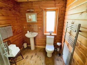A compact wooden cabin bathroom with a sink, toilet, and a window. - Deveron Valley Cottages (Huntly)