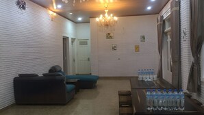 Una habitación con paredes de ladrillo blanco, un candelabro, un sofá, una mesa con botellas de agua y una puerta.