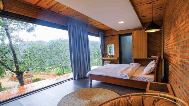 Un dormitorio con un ventanal grande, una cama, una mesita de noche y vistas al verde exterior.