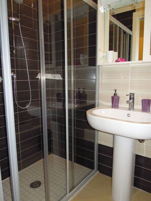 Un baño con ducha de mampara de vidrio, un lavamanos blanco y un espejo sobre él.