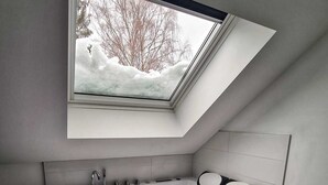 Een moderne badkamer met een dakraam, een bad met een ingebouwde zitplaats en een raam met uitzicht op een besneeerd landschap.