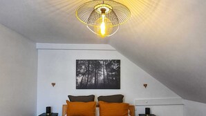 Een slaapkamer met een houten bed, twee nachtkastjes, een aan de muur hangend schilderij en een bijzondere plafondlamp.
