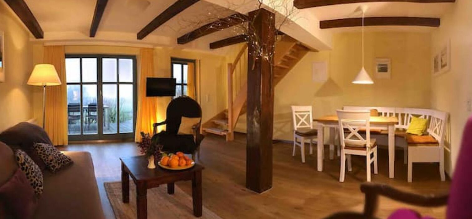 A cozy living room with a sofa, a dining table with chairs, and a staircase leading to an upper level.