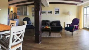 Een ruime woonkamer met een houten eettafel, witte stoelen, een bank en een paarse fauteuil.