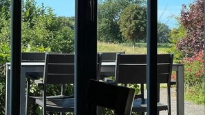 Uitzicht door grote ramen op een terras met zitplaatsen.