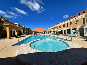 Una piscina amb un centre rebaixat, envoltada d'un pati amb gandules i plantes en testos.