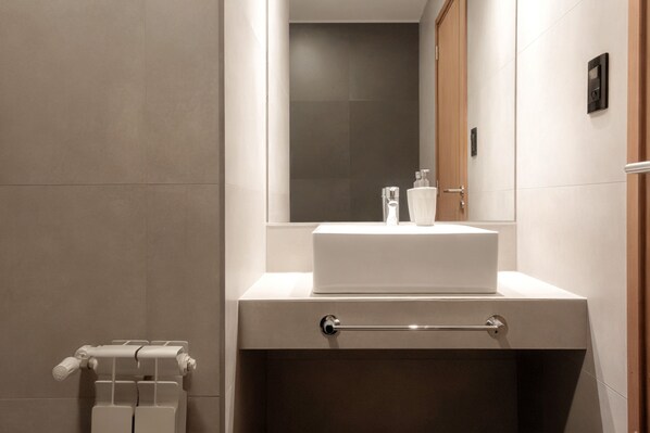 A modern bathroom with a white sink, a mirror above it, and a towel rack to the left.