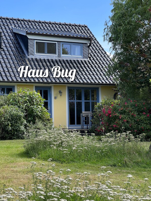 Une maison avec un toit en pente, un grenier apparent et une entrée principale dotée d’une porte et de fenêtres.