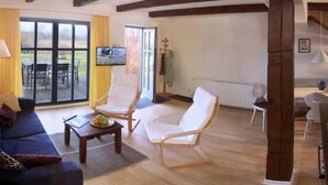 Un salón amplio con un sofá azul, sillones blancos, una mesa de centro de madera y un comedor con una mesa y sillas.