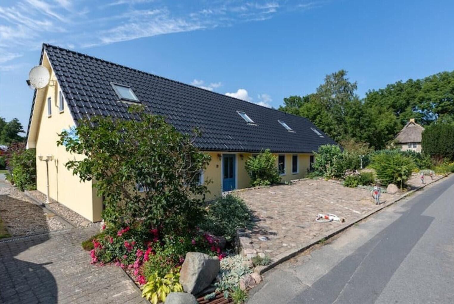 Une maison de plain-pied avec un toit recouvert de tuiles sombres, une porte bleue et une antenne parabolique sur le côté gauche.