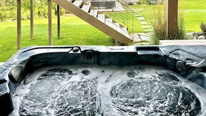Un bain à remous avec vue sur un lac et un escalier menant à une terrasse dotée de parasols.