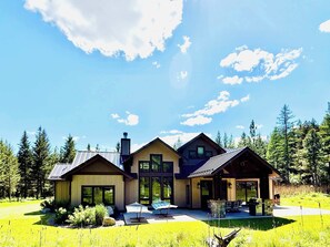 A modern two-story house with a large patio area, surrounded by a forest.