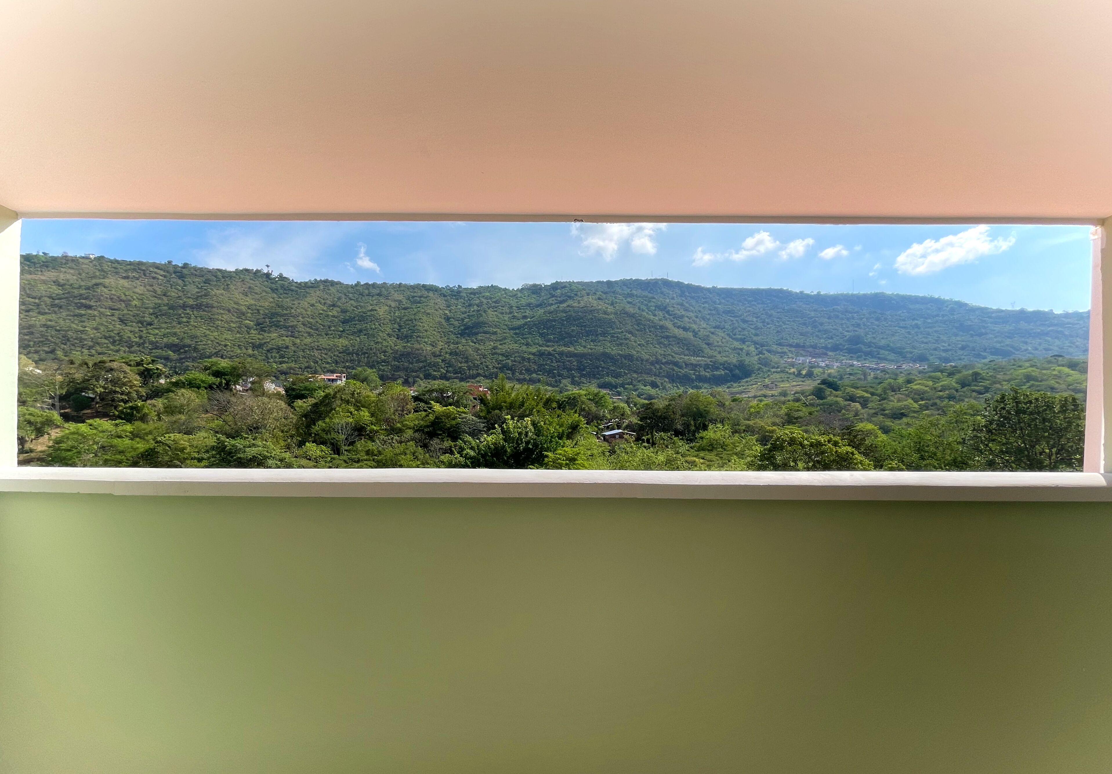 A view from a window overlooking a green landscape with hills and scattered buildings.