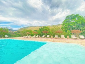 A pool area with lounge chairs and umbrellas, surrounded by greenery and hills. - Trip Monkey del Río (San Gil)