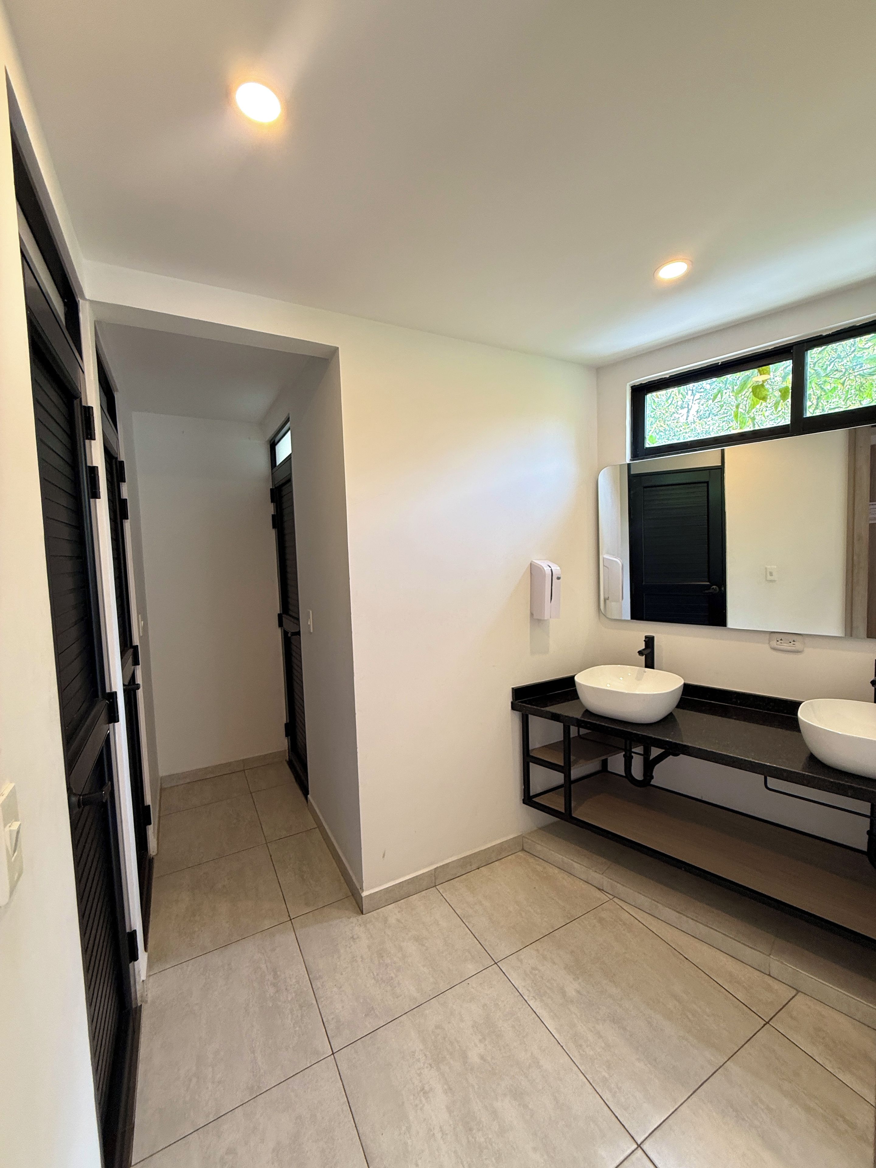 A modern bathroom with a black vanity, two sinks, a mirror, and recessed ceiling lights.