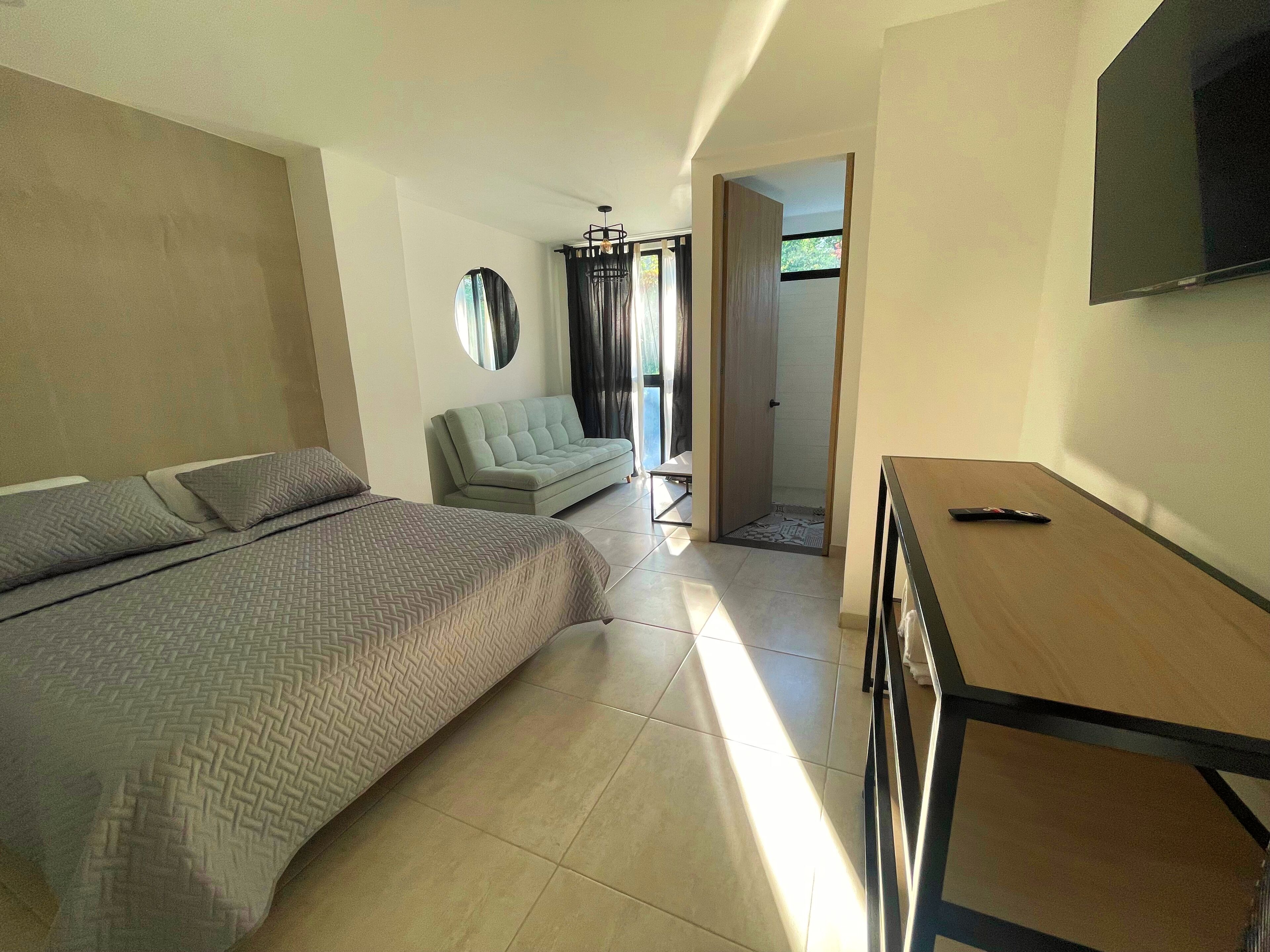 Een slaapkamer met een bed, een bank, een televisie en een deur naar een badkamer.