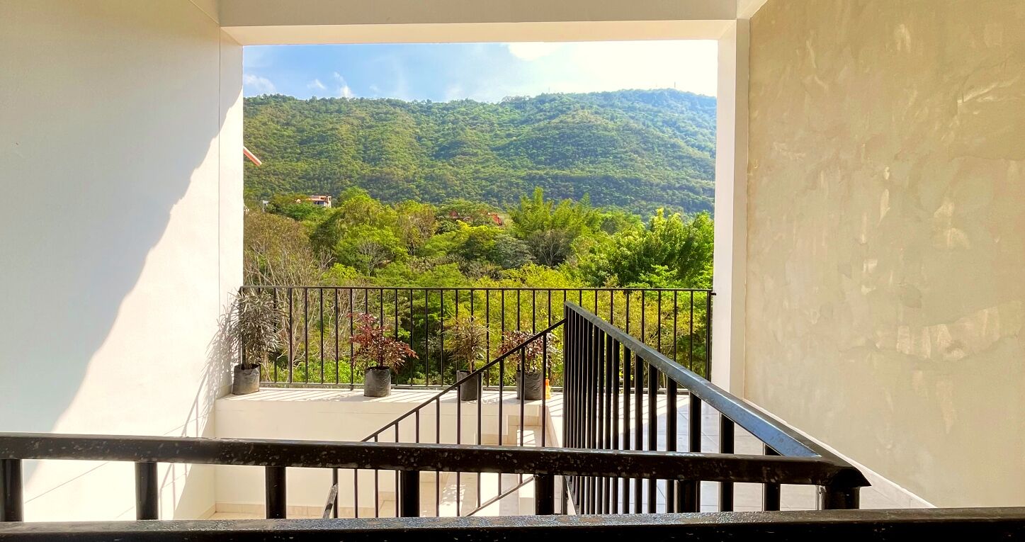 A balcony with a view of a green hillside and a distant building.