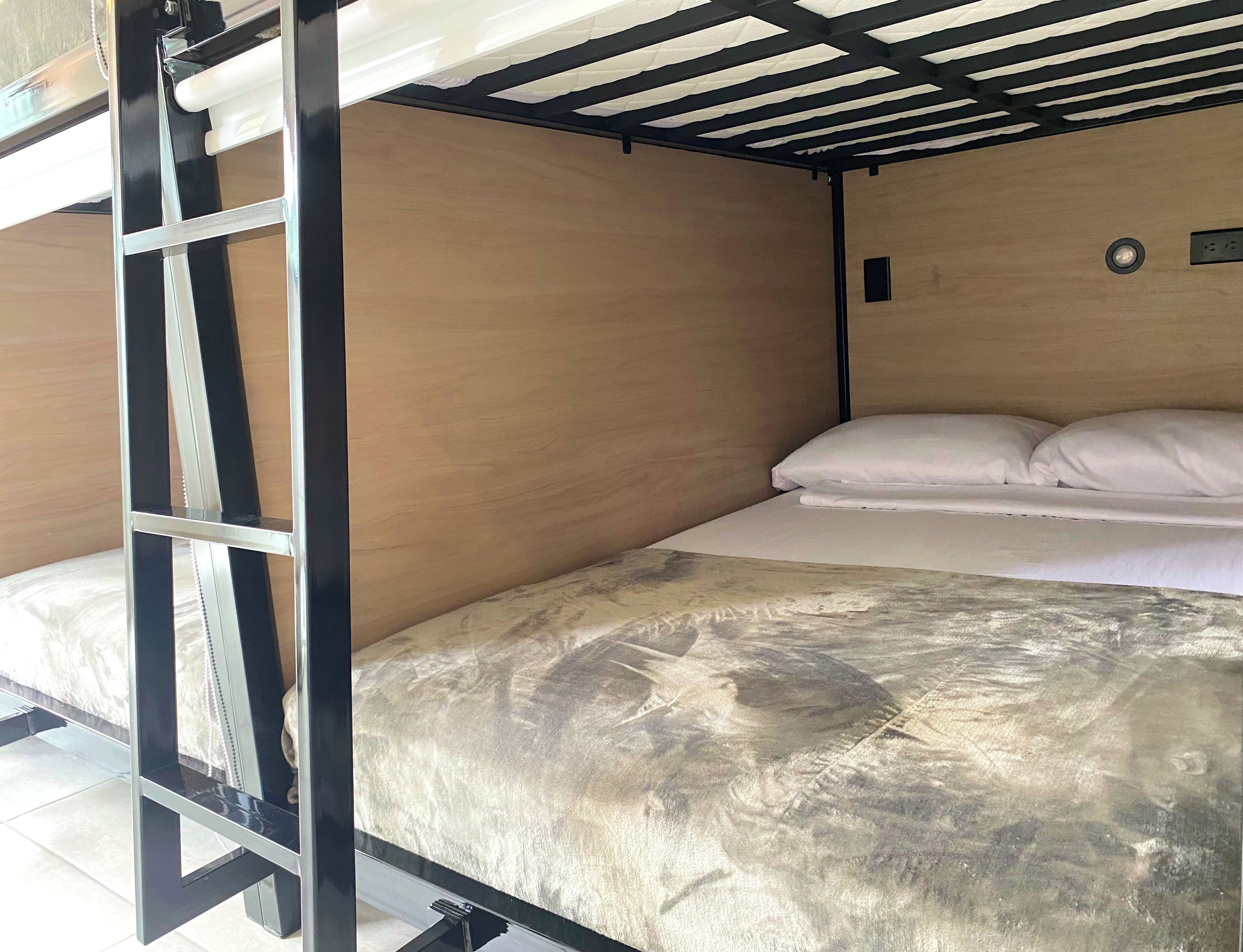 Uma cama beliche com escada, uma cama de solteiro com roupa de cama branca e uma parede de madeira.