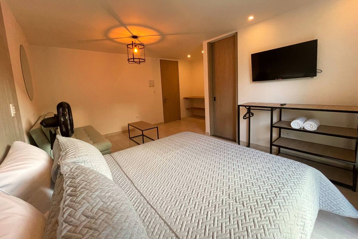 A hotel room with a bed, a TV mounted on the wall, a small table with towels, and a ceiling fan.