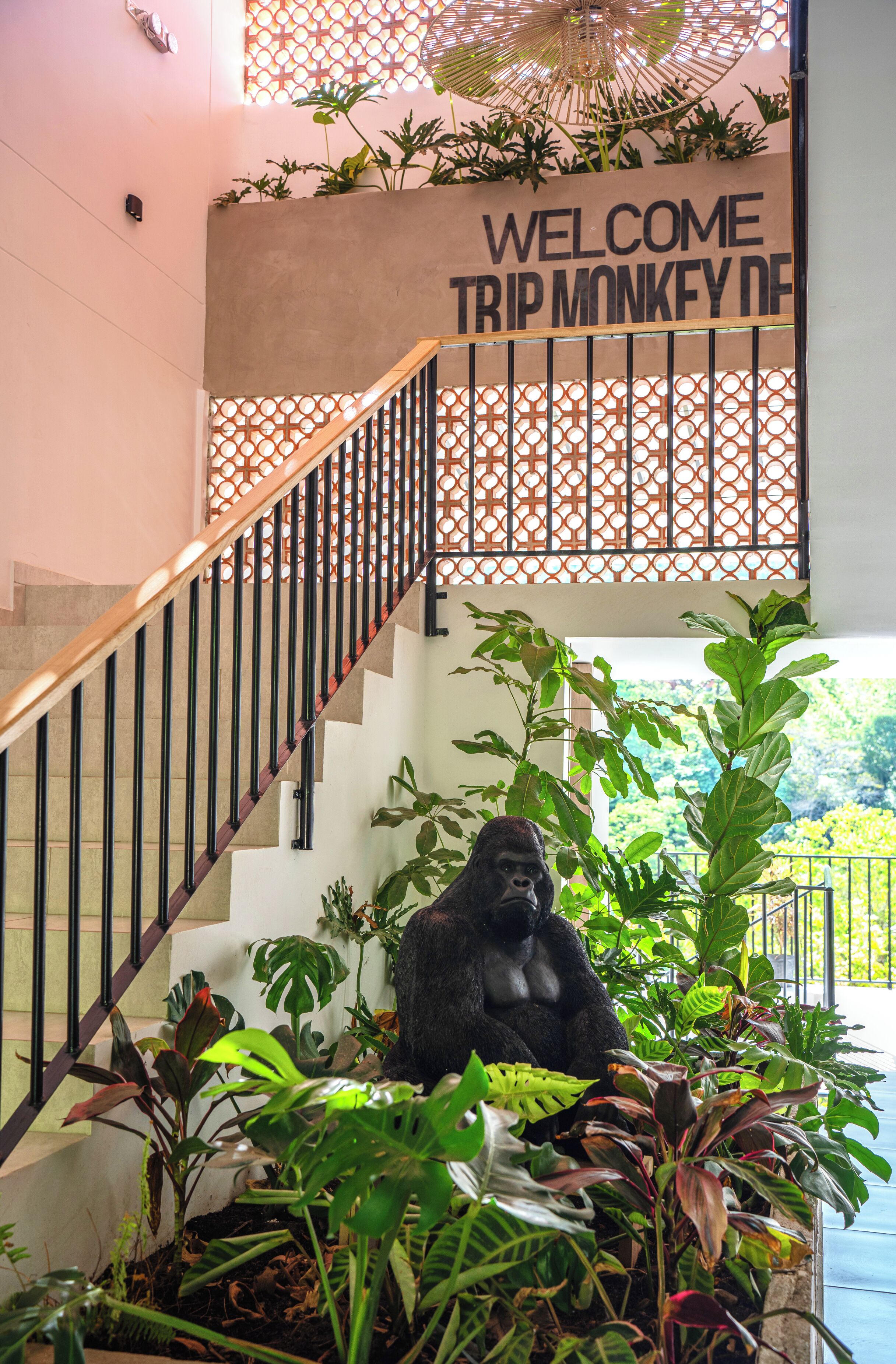 En trappe med en gorilla statue, omgivet af frodige planter, og et skilt med 'Welcome Trip Monkey'.