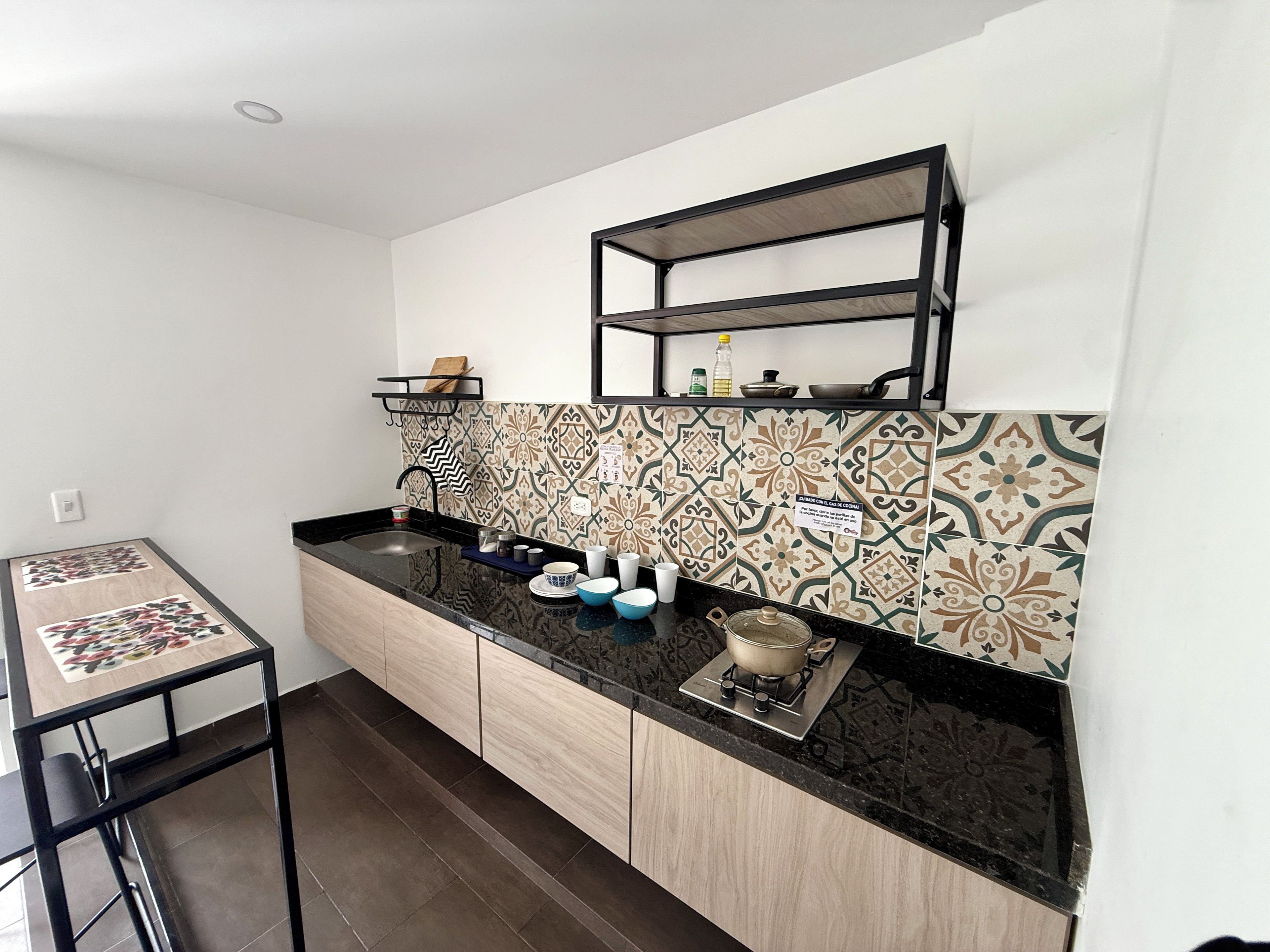 Una cocina con encimera negra, un lavamanos y azulejos decorativos en la pared.