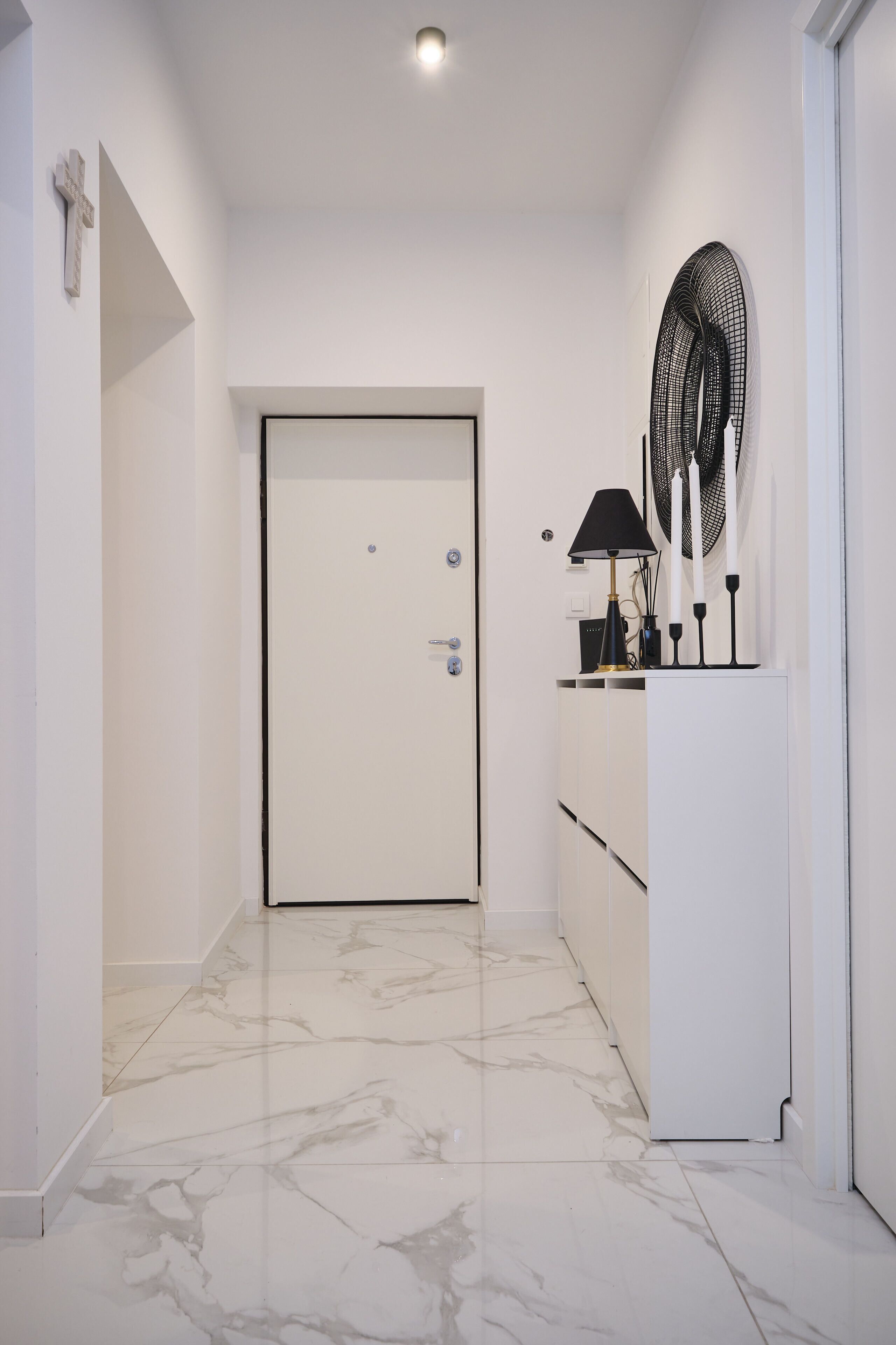 A hallway with a white door, a white cabinet with a fan, and a marble floor.
