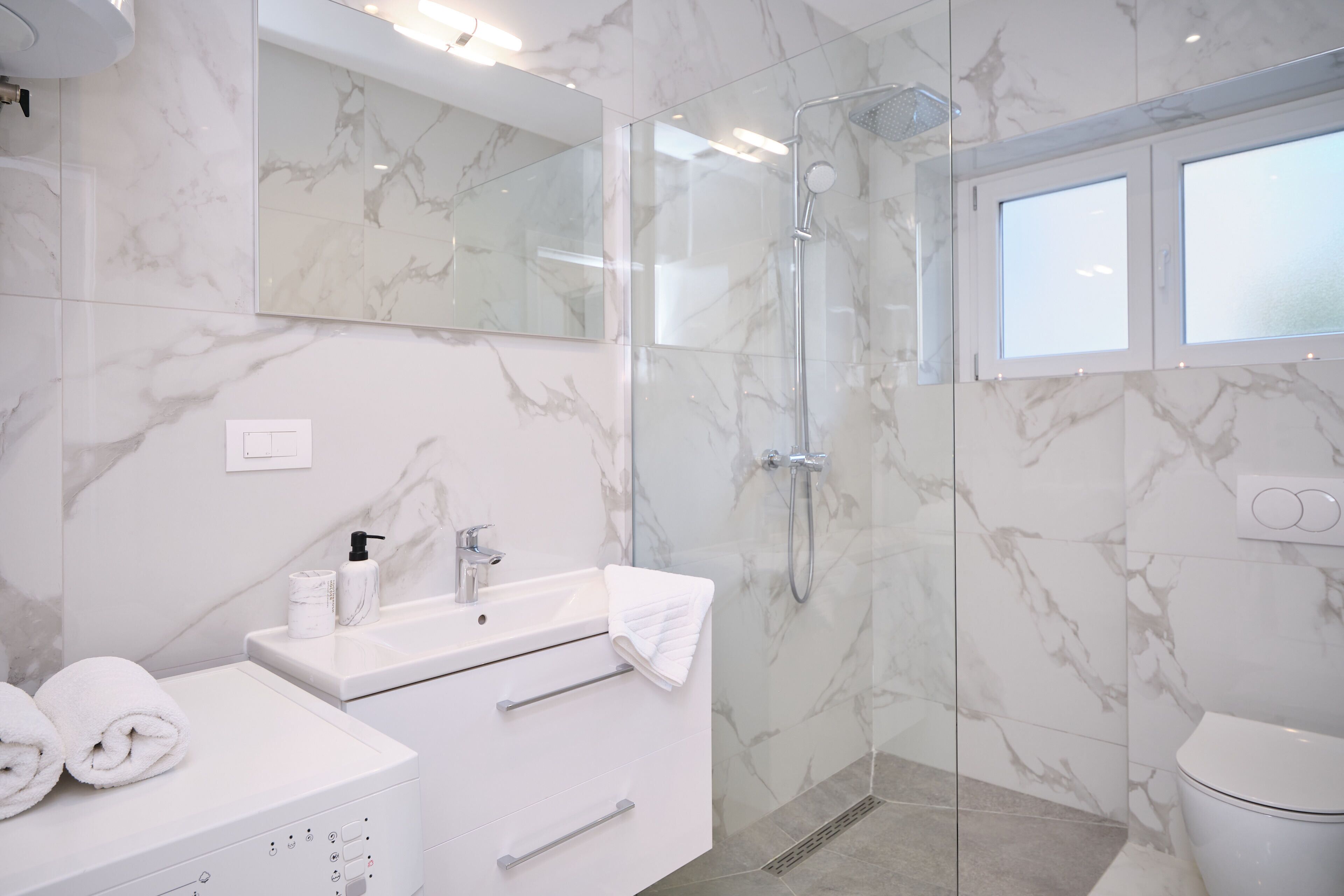 A modern bathroom with a marble sink, a glass-enclosed shower, and a toilet.