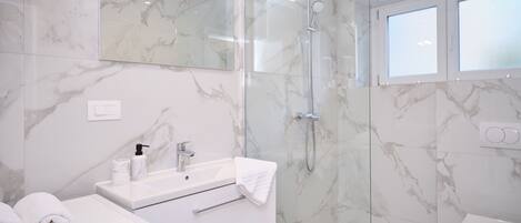 A modern bathroom with a marble sink, a glass-enclosed shower, and a toilet.
