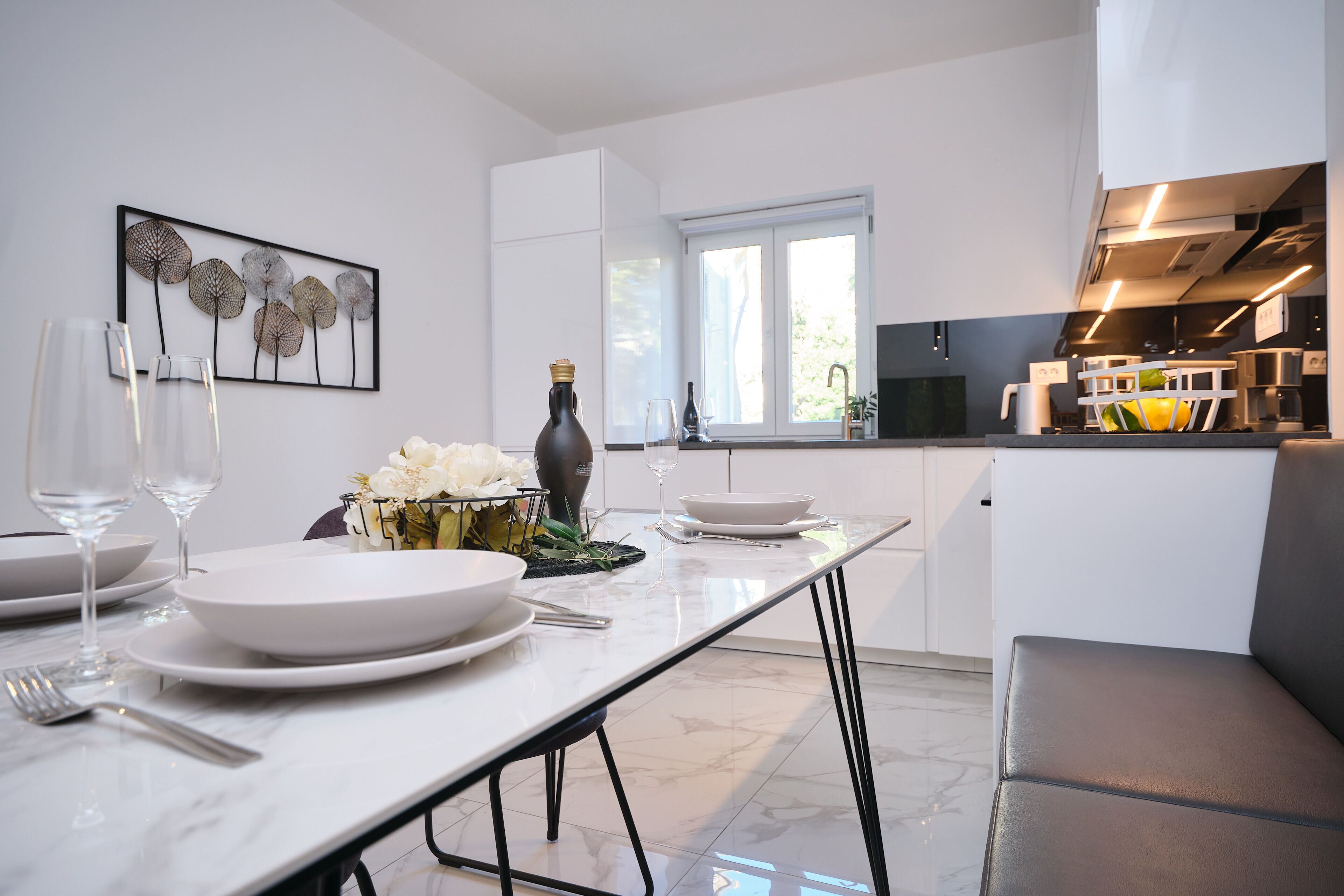 A modern kitchen with white cabinetry, a dining table set with plates and glasses, and a decorative wall piece.