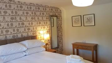 A hotel room with a bed, a nightstand with a lamp, a wooden dresser, and two framed pictures on the wall.