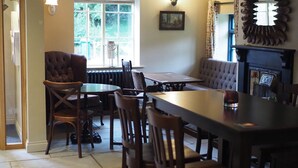 A dining area with a wooden table and chairs, a fireplace, and a window with a view of greenery. - The Star Inn (Driffield)