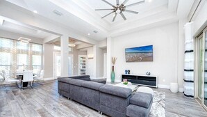 A spacious living room with a grey sectional sofa, a dining area with a table and chairs, and a large painting on the wall. - Venice 3 bedroom contemporary home with pool/spa and close to beautiful beaches (Venice)