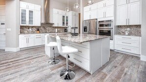 A modern kitchen with white cabinetry, granite countertops, stainless steel appliances, and a central island with bar stools. - Venice 3 bedroom contemporary home with pool/spa and close to beautiful beaches (Venice)