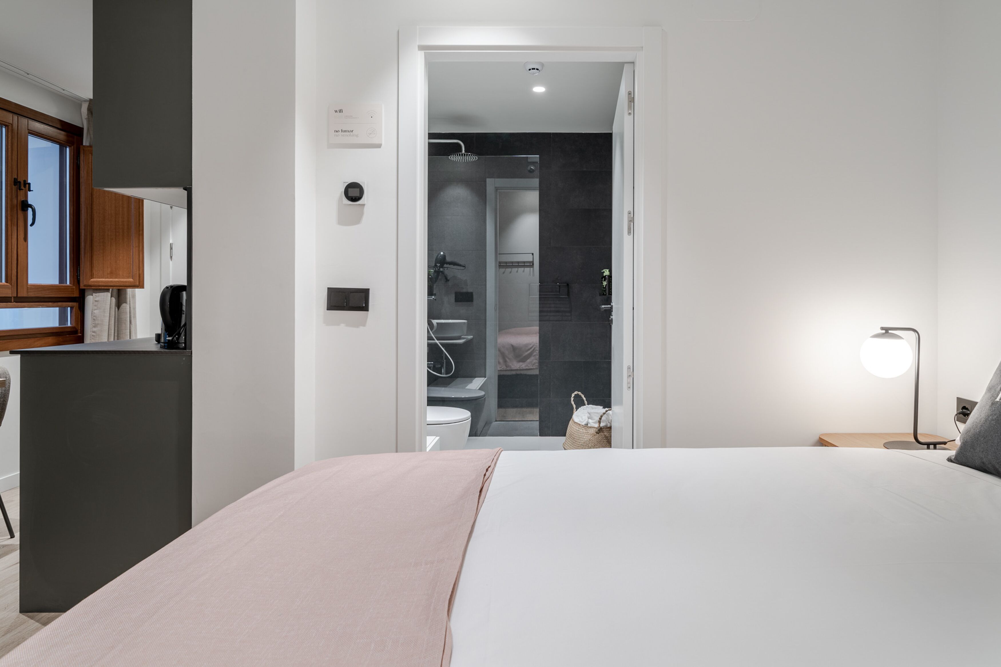 A modern hotel room with a bed, bedside table, and a view into the bathroom.