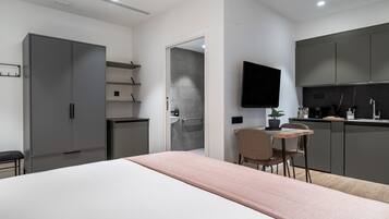 A modern bedroom with a bed, a bedside table, a chair, a TV, and a kitchenette.
