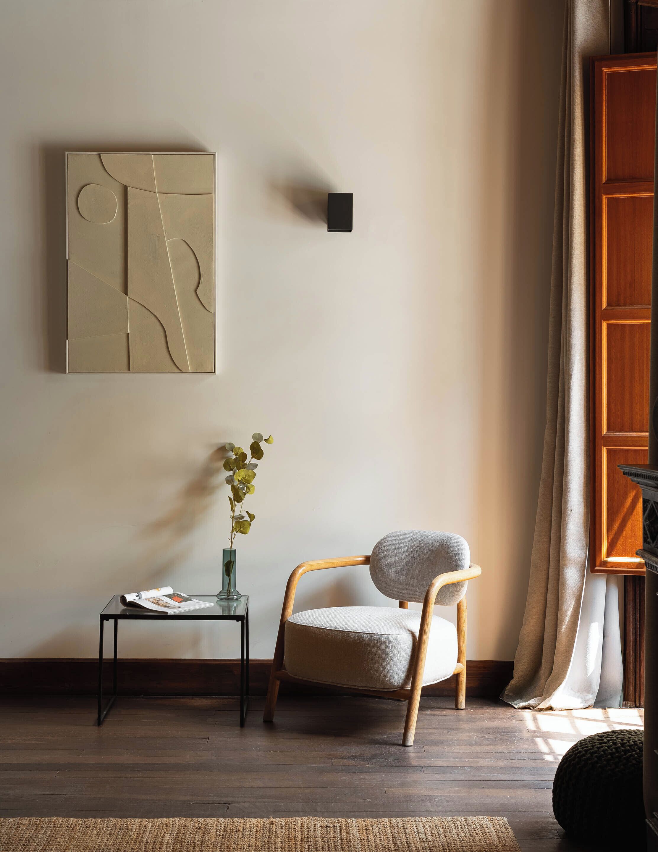 Une pièce comprenant une chaise en bois, une petite table avec un vase et une œuvre d’art abstraite accrochée au mur.