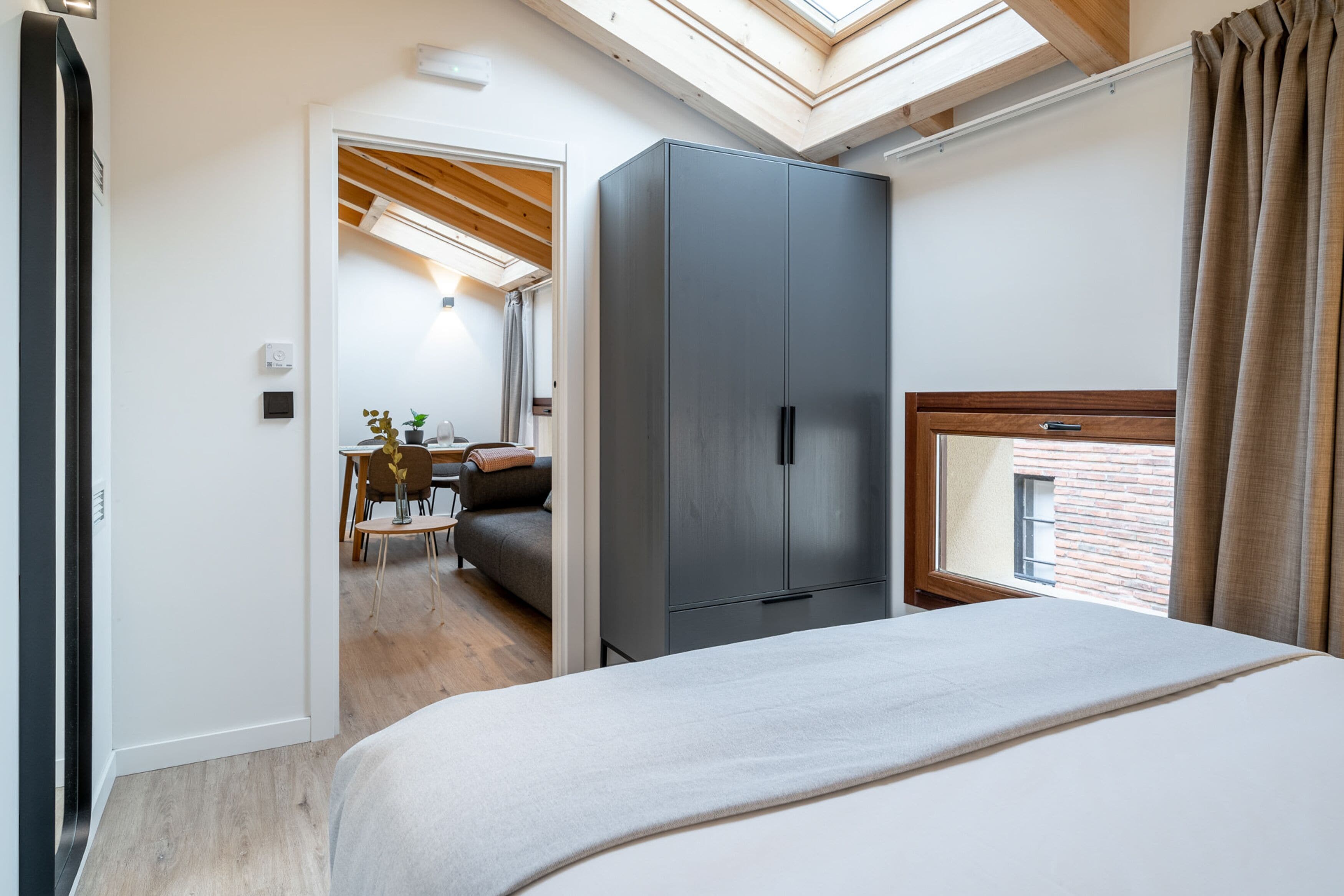 Een slaapkamer met dakraam, een garderobe, een bed en uitzicht op een gebouw van baksteen.