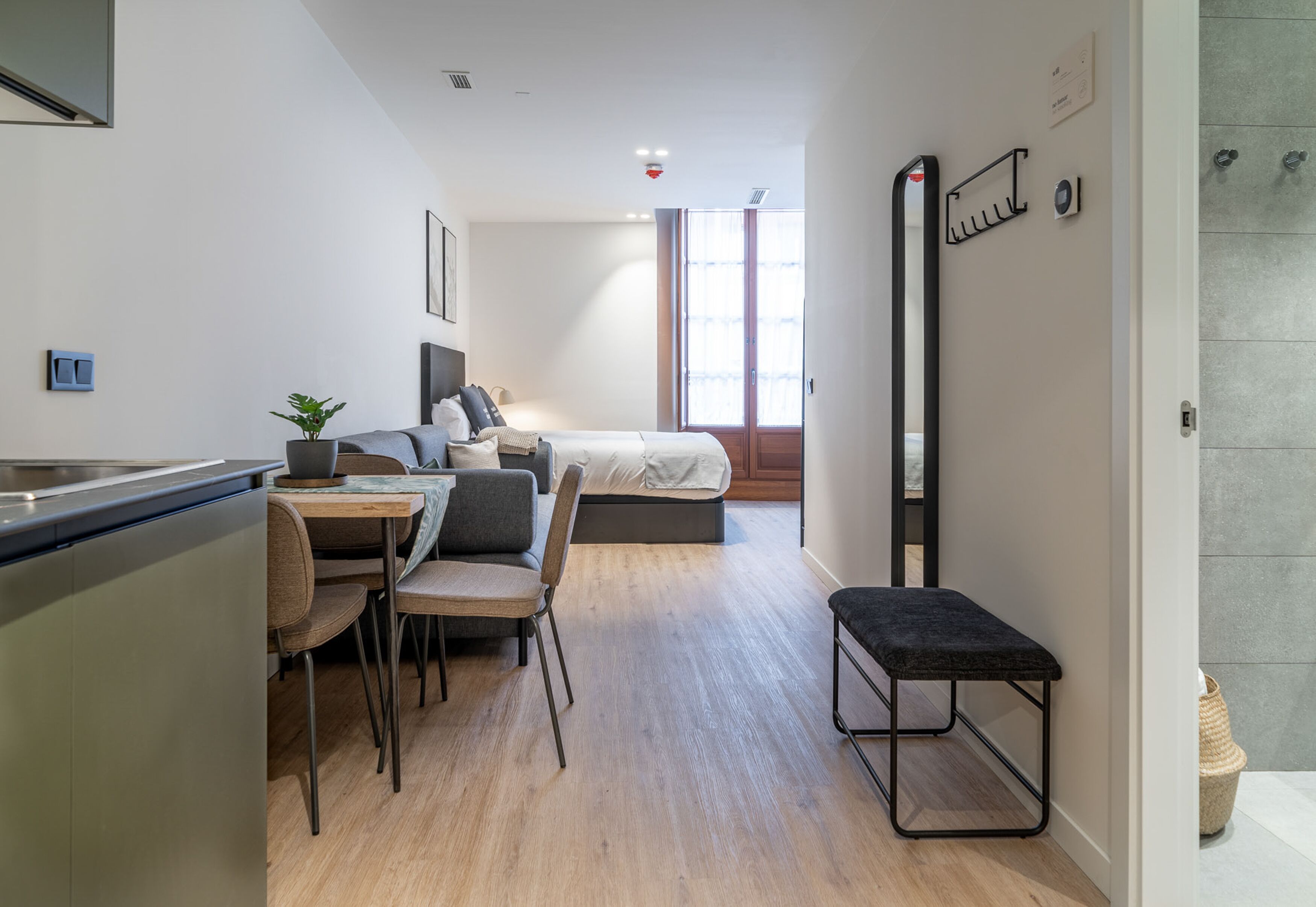 Una habitación de hotel moderna y compacta con kitchenette, comedor, cama y baño.
