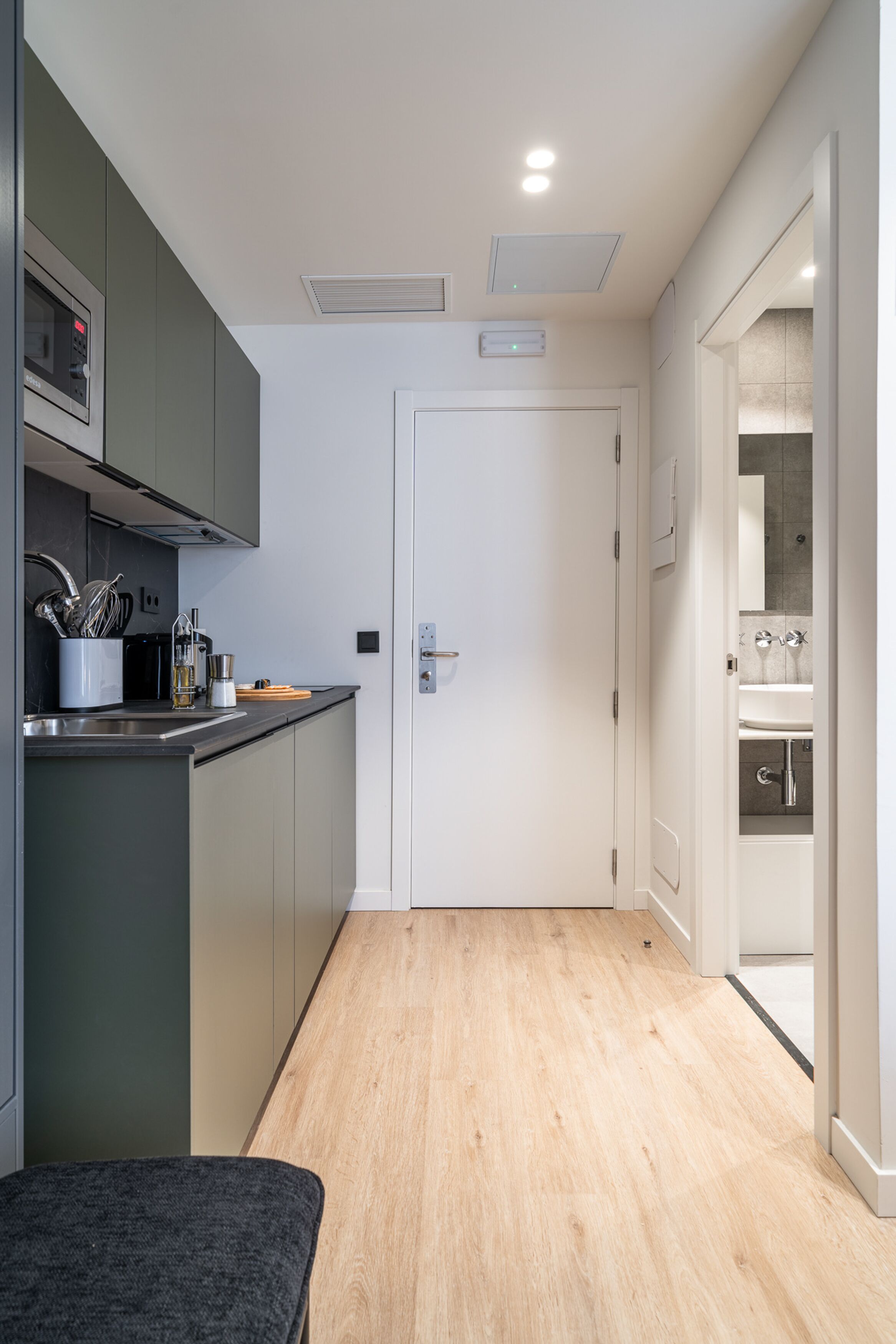 Una cocina moderna con armarios grises, una encimera de madera y una puerta blanca que da a un baño.