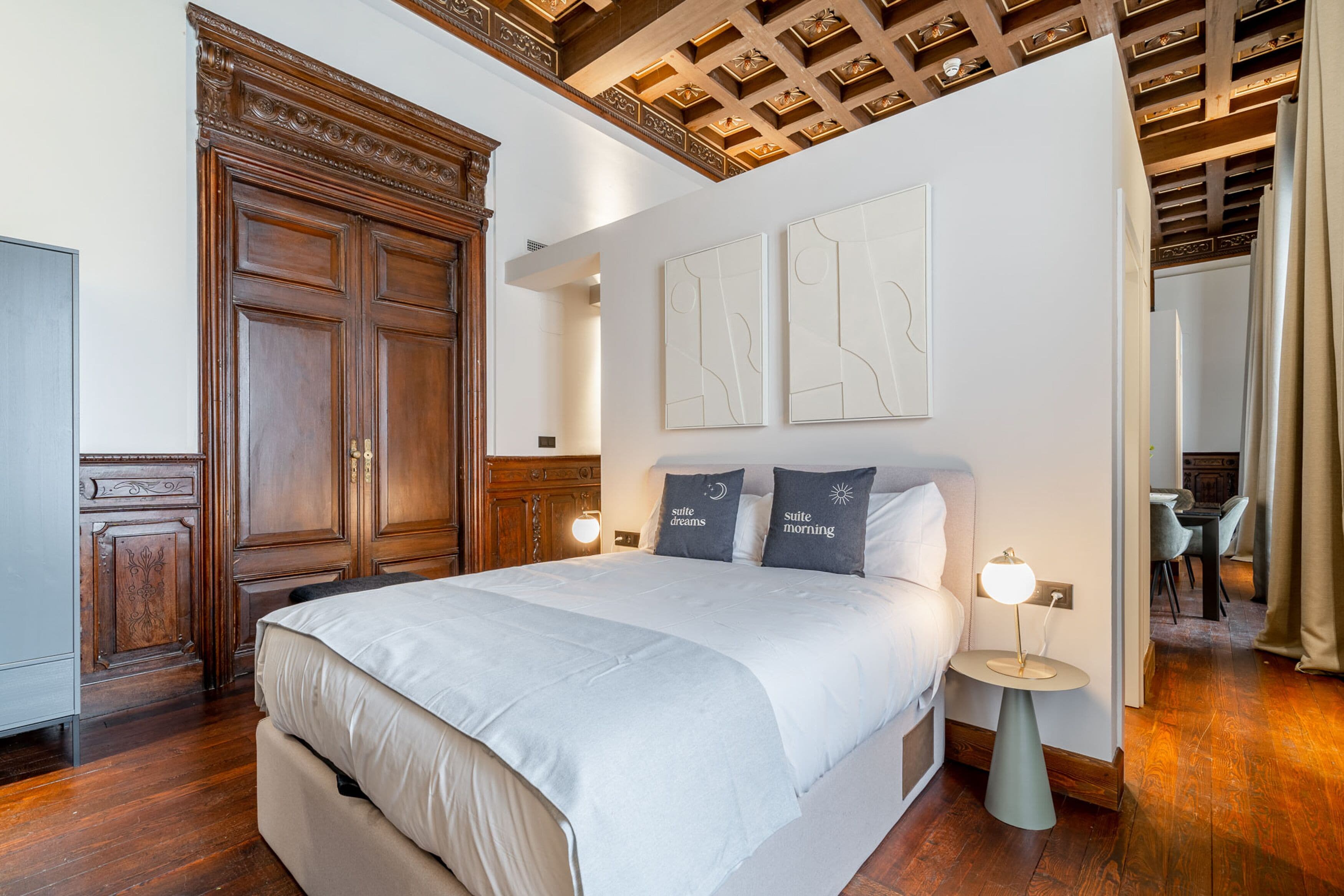 A hotel room with a large bed, wooden wardrobe, and a ceiling with intricate woodwork.