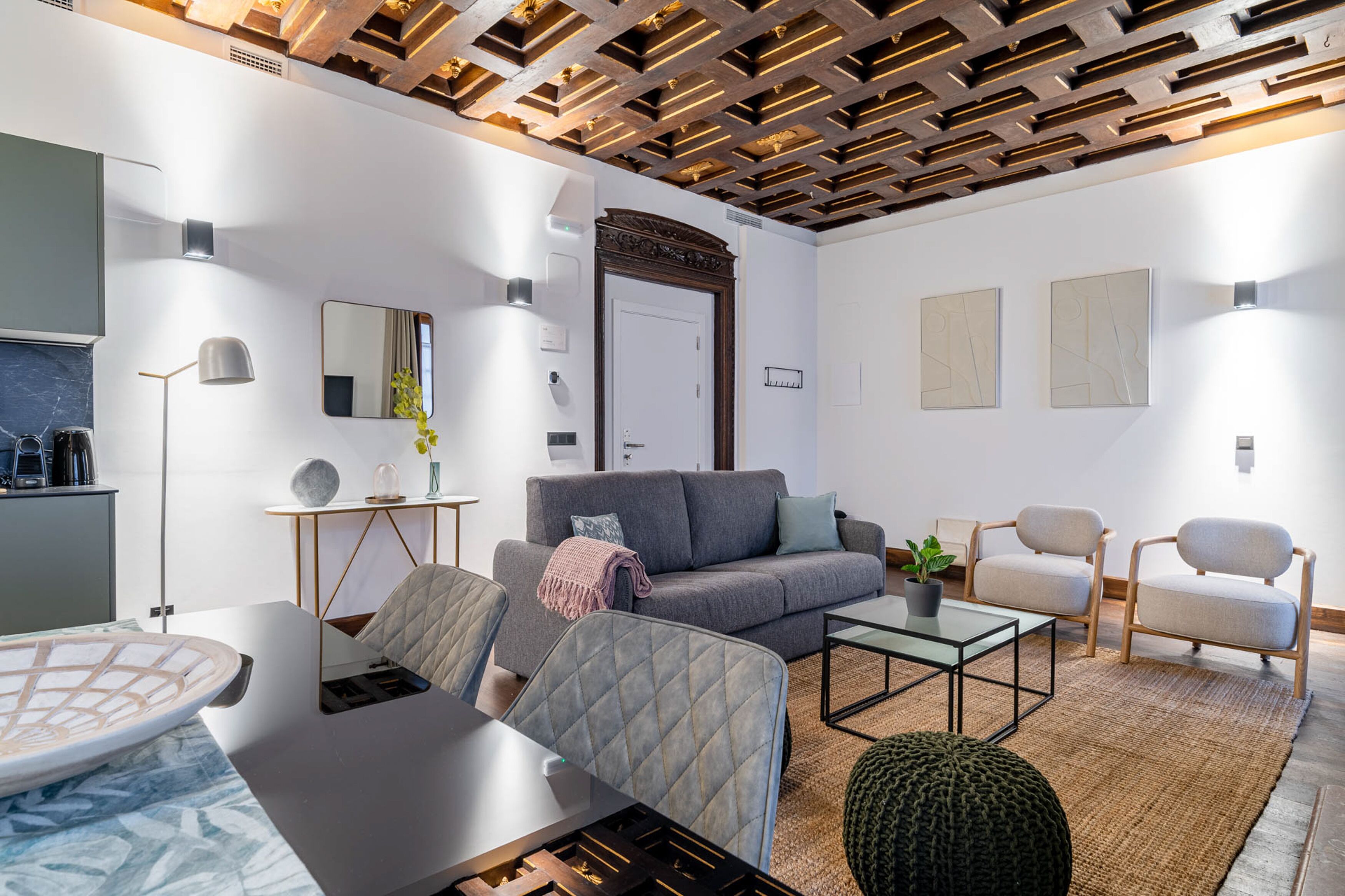 Una sala de estar moderna con un sofá gris, dos sillones, una mesa de centro y un comedor con mesa y sillas de vidrio.