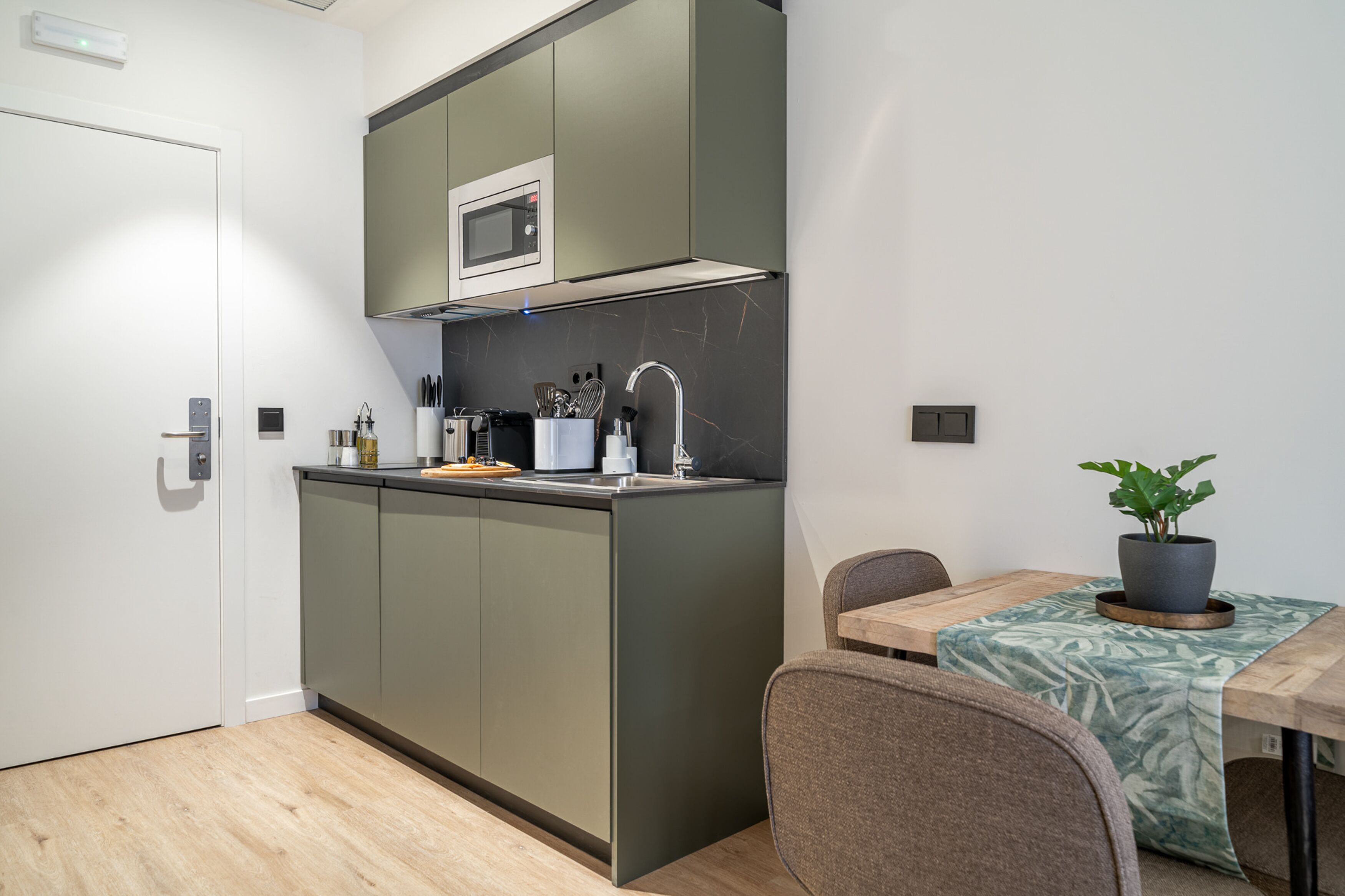 A compact kitchen with a microwave, sink, and a dining area with a table and chairs.