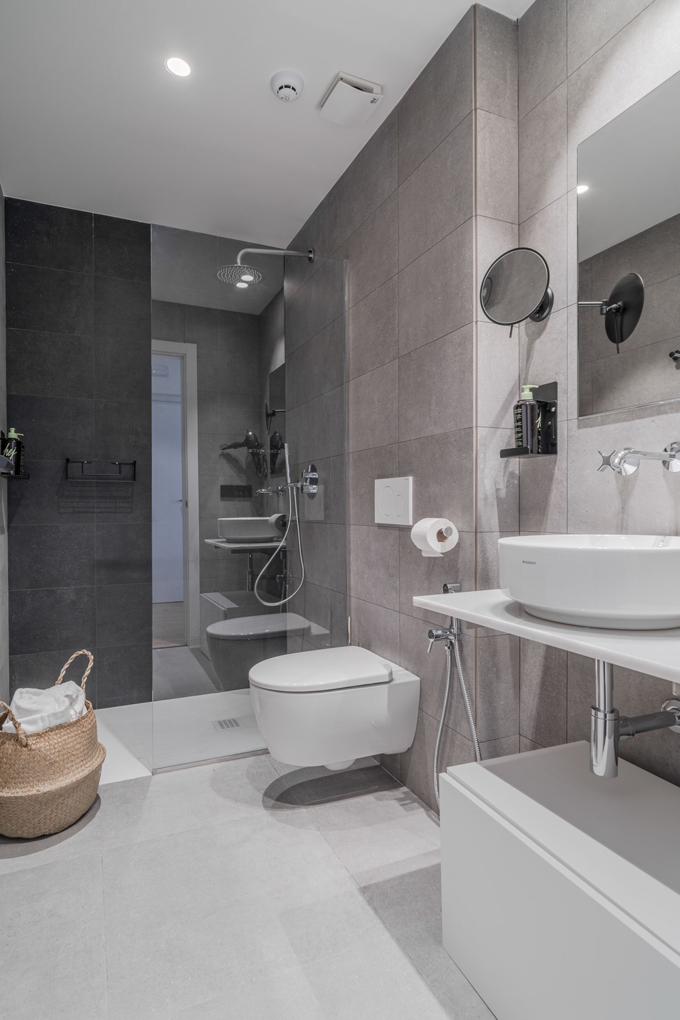 A modern bathroom with a glass-enclosed shower, a toilet, a sink, and a mirror.